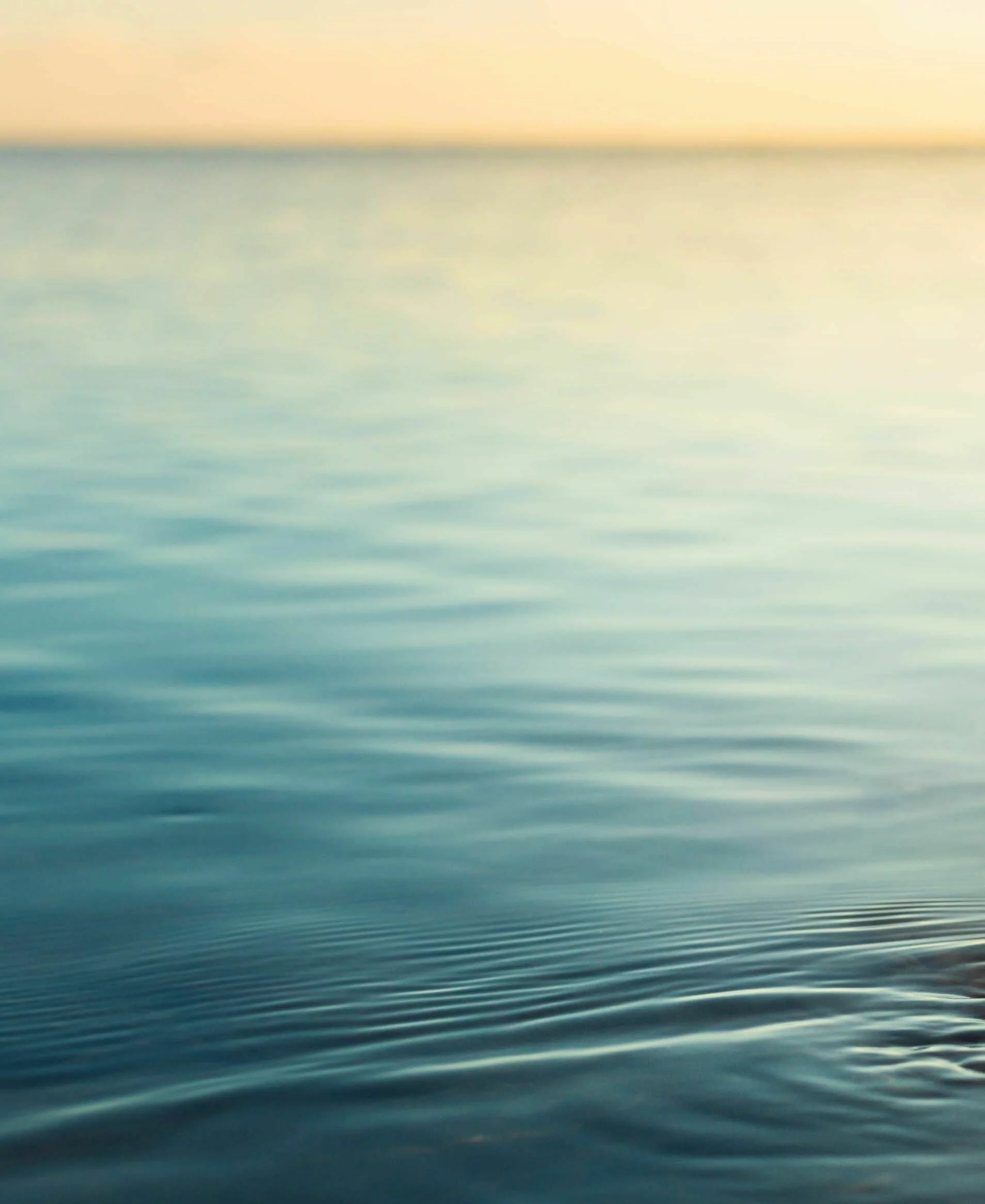 Menschenhand taucht in ruhiges Meerwasser bei Sonnenuntergang.